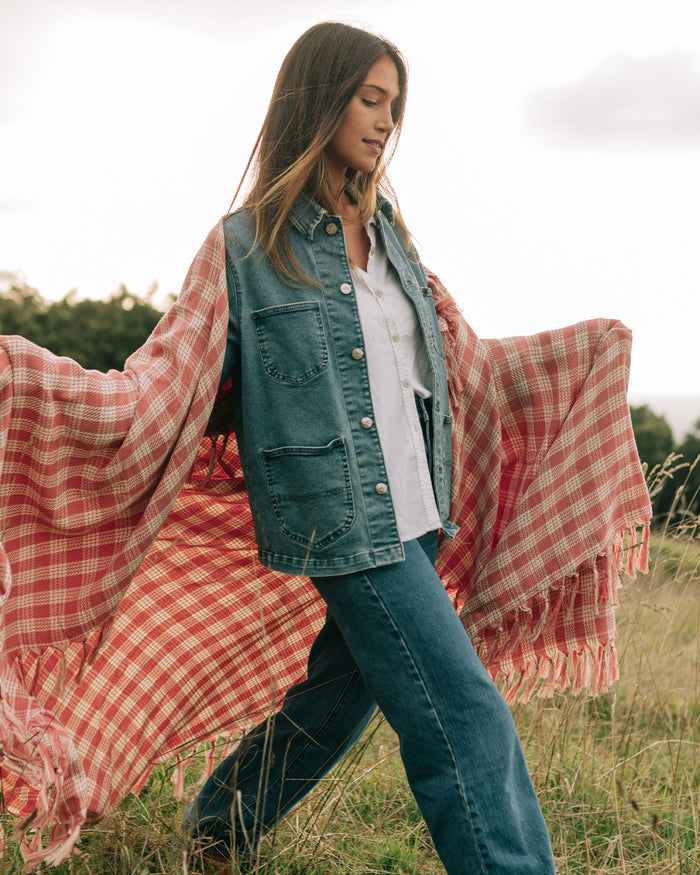 Model holding the Slowtide Palaka Lightweight Beach Blanket in guava open in a field, wearing jeans and a denim vest.