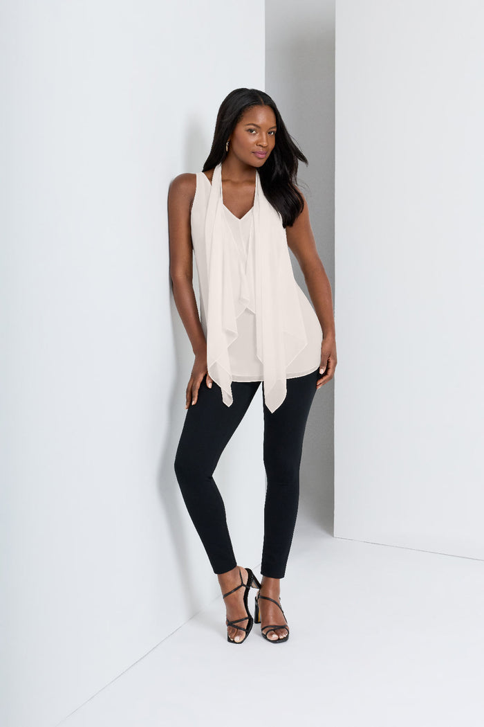 Woman next to wall wearing a white tunic blouse with black leggings