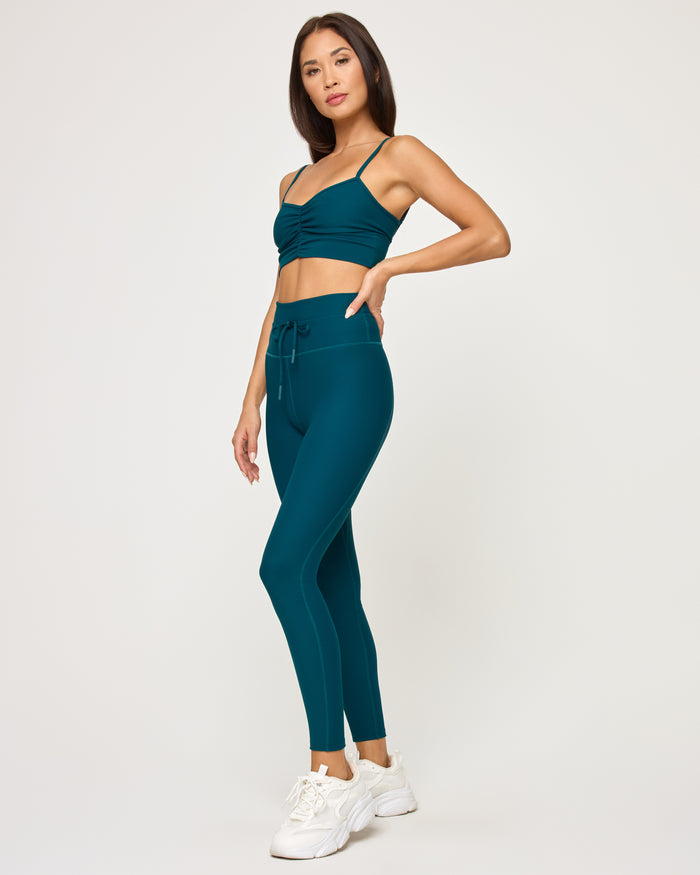 Side view of model wearing the Soren Top in deep teal with matching deep teal Turner Legging and white sneakers.