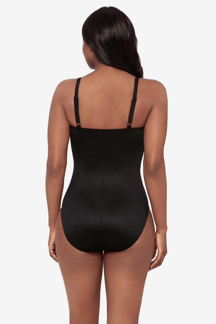 Woman turned away wearing a green and white feather printed one-piece swimsuit