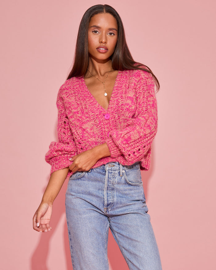 Close-up front view of a model wearing the LSPACE Strawberry Fields Cardigan in strawberry marl, showing the pink marl cable-knit texture and V-neckline against a pink background.