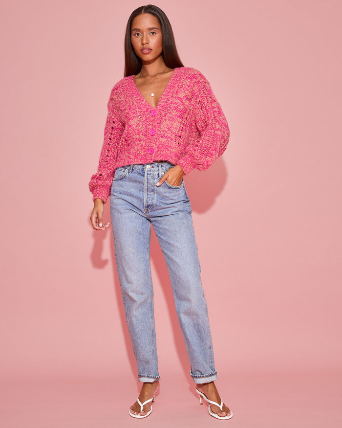 Full-length front view of a model wearing the LSPACE Strawberry Fields Cardigan in strawberry marl, styled open over a white tee with jeans and white strappy sandals on a pink background.