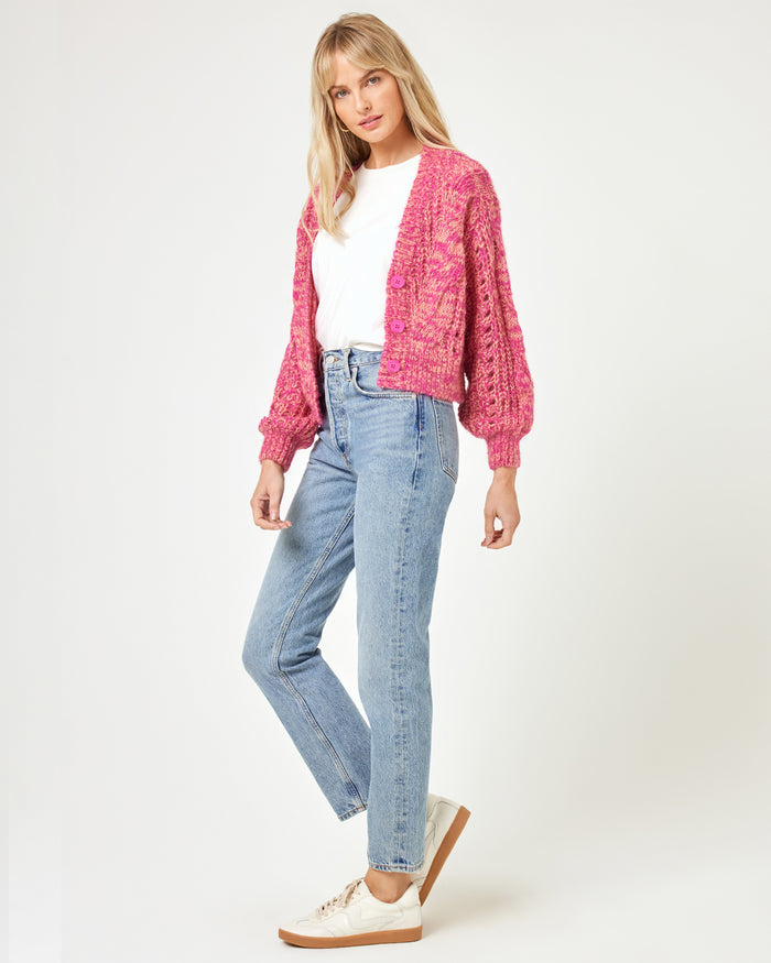 Side view of a model wearing the LSPACE Strawberry Fields Cardigan in strawberry marl, showing the relaxed cable-knit silhouette styled with jeans and sneakers on a white background.