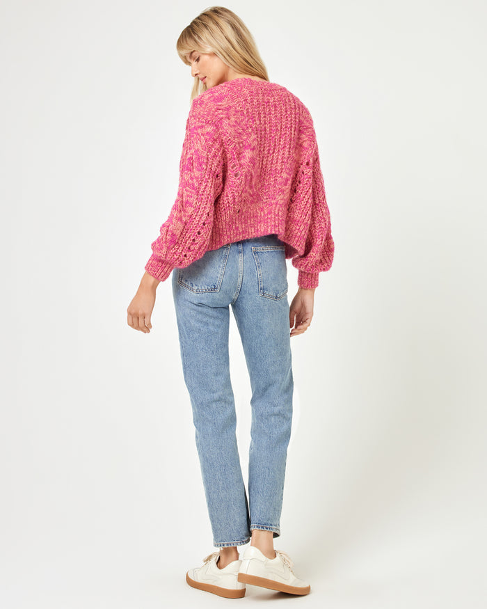 Back view of a model wearing the LSPACE Strawberry Fields Cardigan in strawberry marl, showing the pink cable-knit back and long sleeves on a white background.
