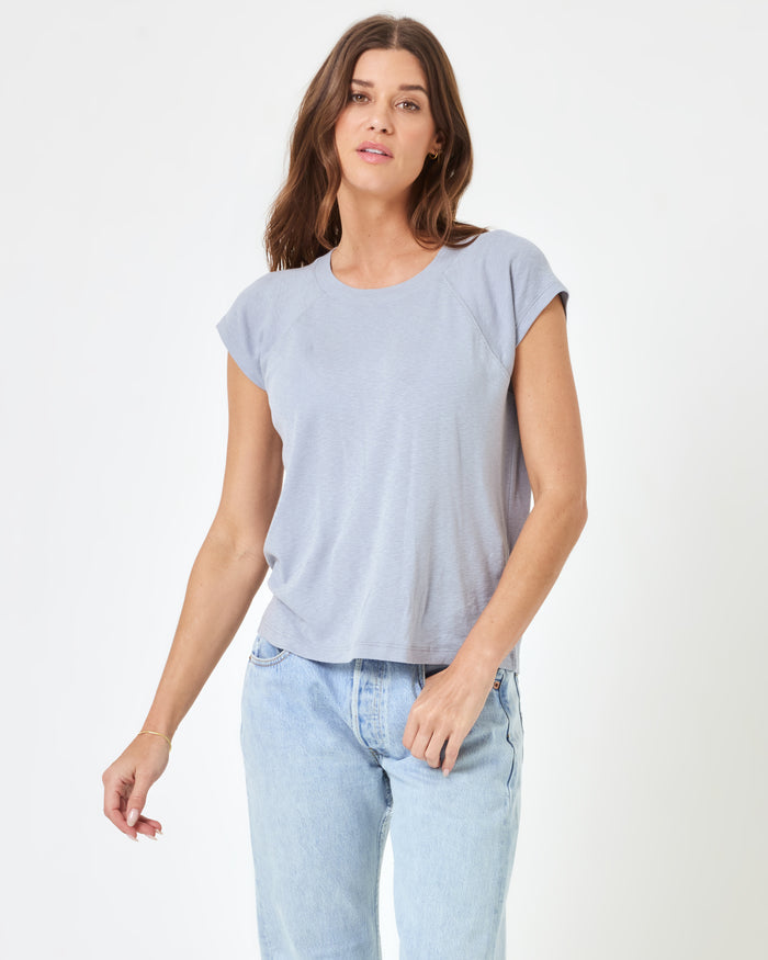 Front view of a model wearing the LSPACE Sunday Tee in haze, a soft lavender-grey short-sleeve boxy crop tee with a scoop neckline and raglan sleeves, paired with light wash jeans.