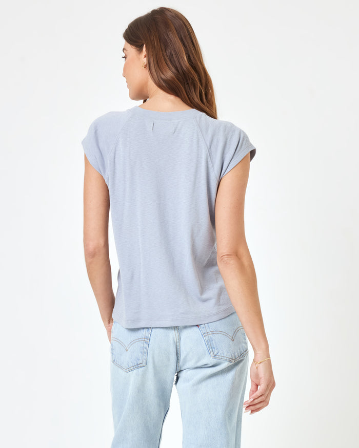 Back view of a model wearing the LSPACE Sunday Tee in haze, a soft lavender-grey short-sleeve boxy crop tee with raglan sleeves, paired with light wash jeans.