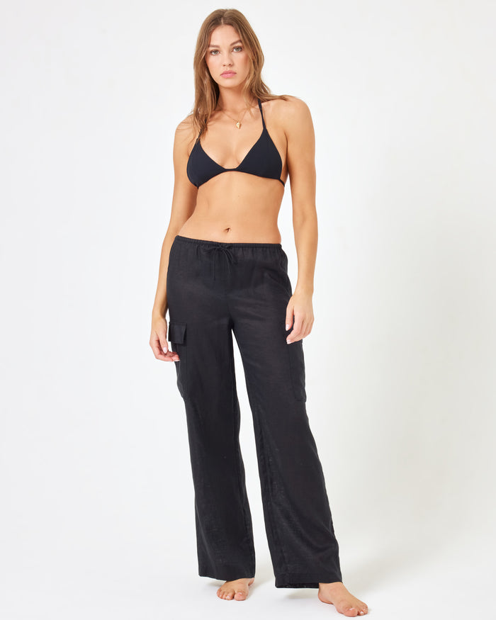 Close-up front view of a model wearing the LSPACE Sundown Cargo Pant in black, highlighting the cargo pocket hardware and waistband detail.