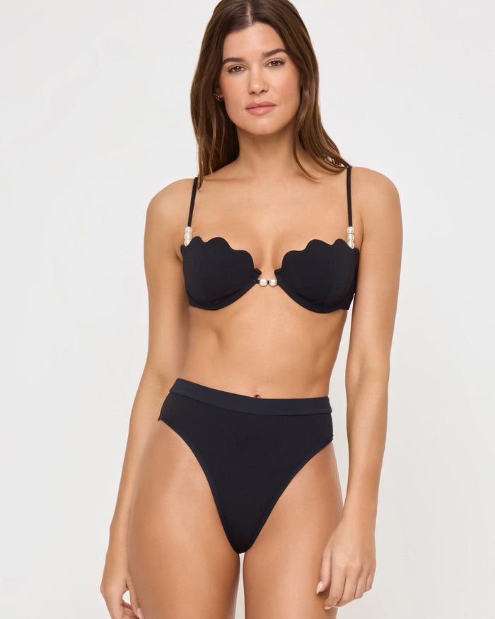Front view of a model wearing the LSPACE black Sunrise Shell Bikini Top, a scalloped underwire style with pearl hardware, paired with a black high-waist Frenchi Bikini Bottom.