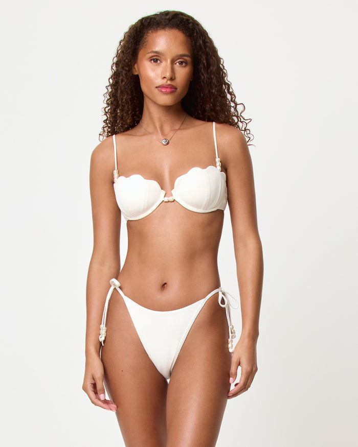 Front view of a model in a studio wearing the LSPACE cream Sunrise Shell Bikini Top and Lucia Bikini Bottom with pearl tassel side ties, paired with a cream scalloped shell bikini top.