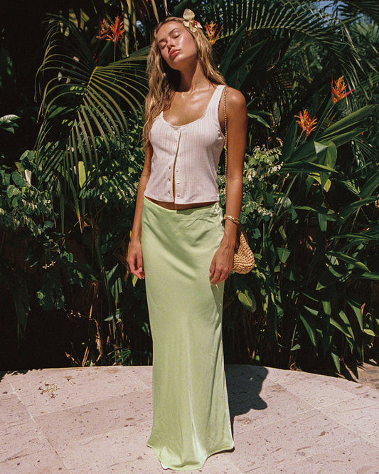 Front view of a model wearing the LSPACE Sweet As Honey Skirt in honeydew, a satin maxi skirt with a bias-cut silhouette, styled in a tropical garden setting.