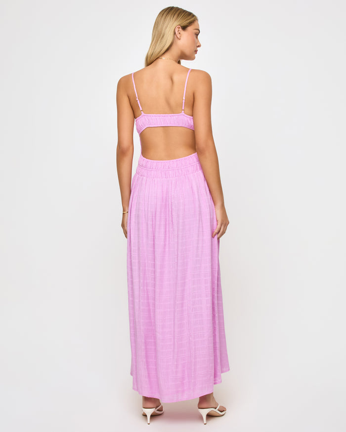 Back view of a model wearing the LSPACE Tala Dress in light iris, showing the wide open-back cutout between the bodice and smocked waistband of the lavender maxi dress.
