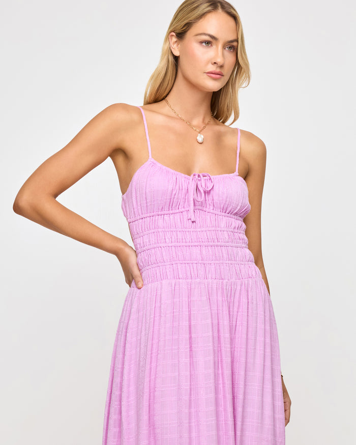 Close-up of a model wearing the LSPACE Tala Dress in light iris, highlighting the smocked bodice and front center tie with tassel detail on the soft lavender maxi dress.