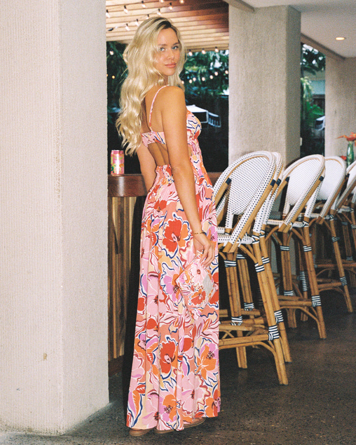 Campaign back view of a model wearing the LSPACE Tala Dress in lost in the blooms, showing the open-back cutout of the vibrant floral maxi dress, photographed in an indoor bar setting.