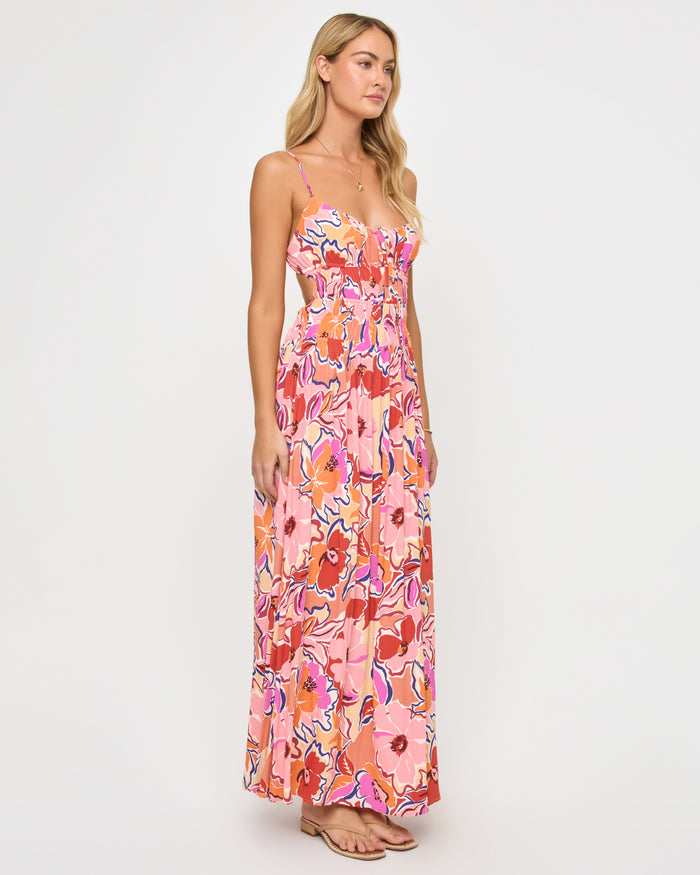 Angled view of a model wearing the LSPACE Tala Dress in lost in the blooms, showing the side open-back cutout of the retro floral maxi dress with the vibrant pink, orange, and red bloom print.