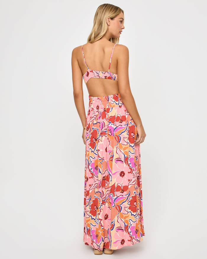 Back view of a model wearing the LSPACE Tala Dress in lost in the blooms, showing the wide open-back cutout of the retro floral maxi dress in the vibrant pink, orange, red, and blue print.