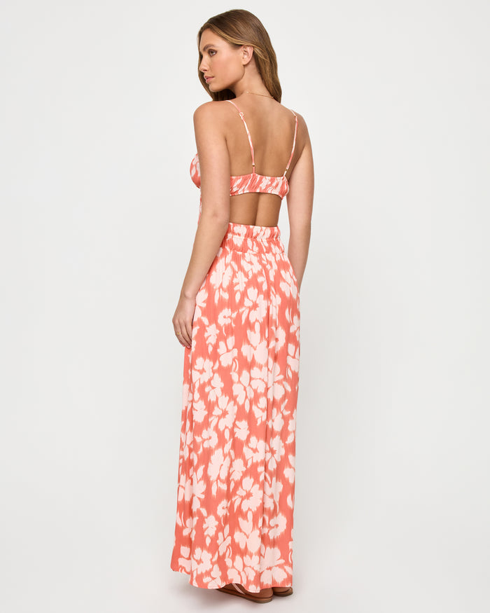 Back view of a model wearing the LSPACE Tala Dress in vine vignette, showing the open back with spaghetti straps and an open back cutout above the smocked waist in a coral and white floral print.