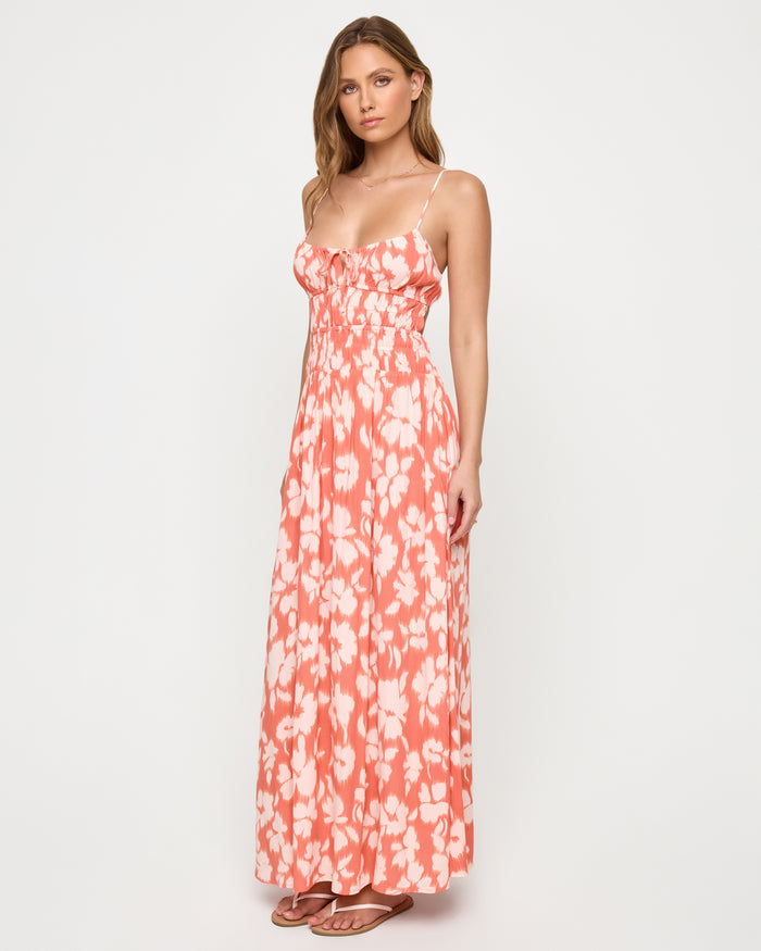 Three-quarter front view of a model wearing the LSPACE Tala Dress in vine vignette, showing the spaghetti straps, front tie bodice detail, and flowing maxi skirt in a coral and white floral print.