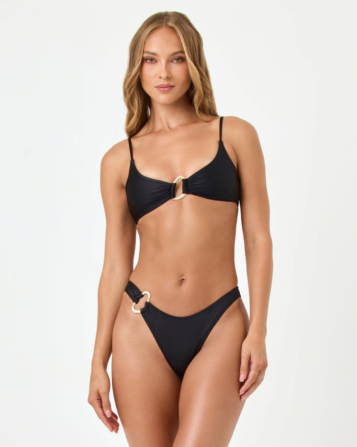 Front view of a model wearing the LSPACE black Teagan Bikini Bottom with gold ring hardware detail.