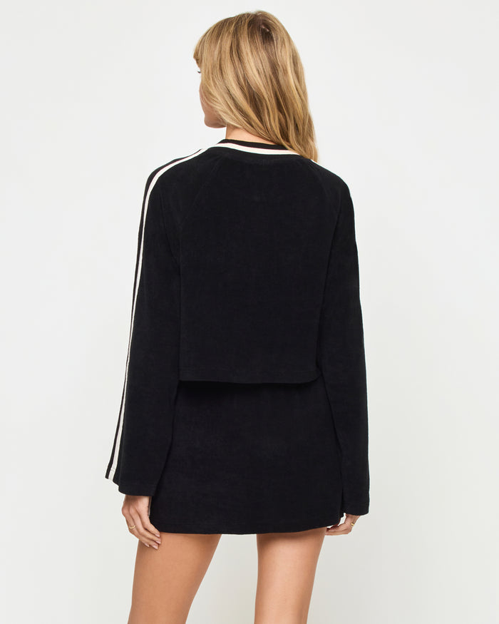 Back view of the LSPACE Tempo Pullover in black-cream on a model against a light background, showing the back of the cropped crew-neck sweatshirt with cream stripe detail, paired with the matching black-cream mini active skort.