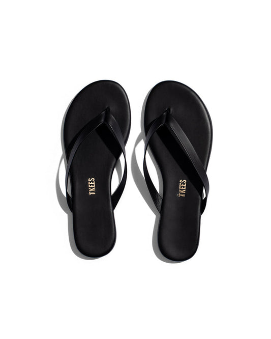 Top view of the TKEES Boyfriend Sandals in black, showing a pair of flat thong sandals with a thin strap and round toe.