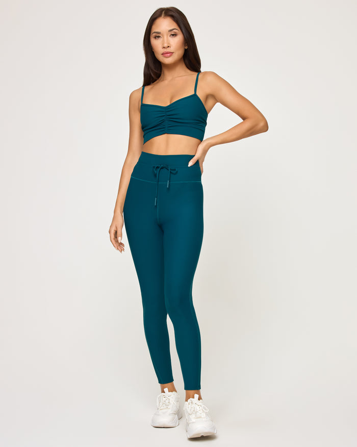 Front view of model wearing the Turner Legging in deep teal with matching deep teal Soren Top and white sneakers.