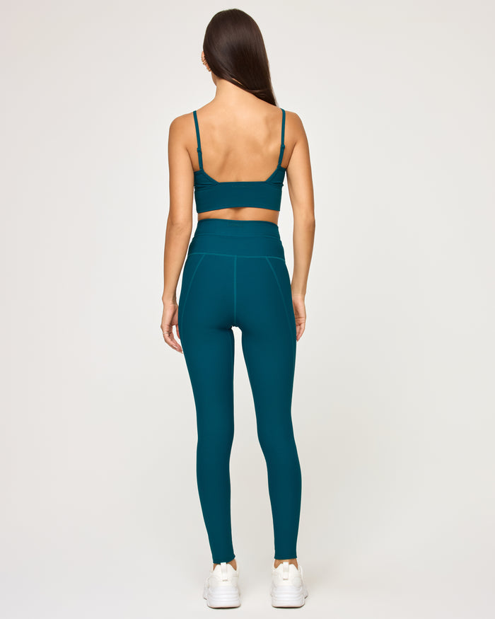 Back view of model wearing the Turner Legging in deep teal showing the high-waist back seam detail, with matching deep teal Soren Top and white sneakers.