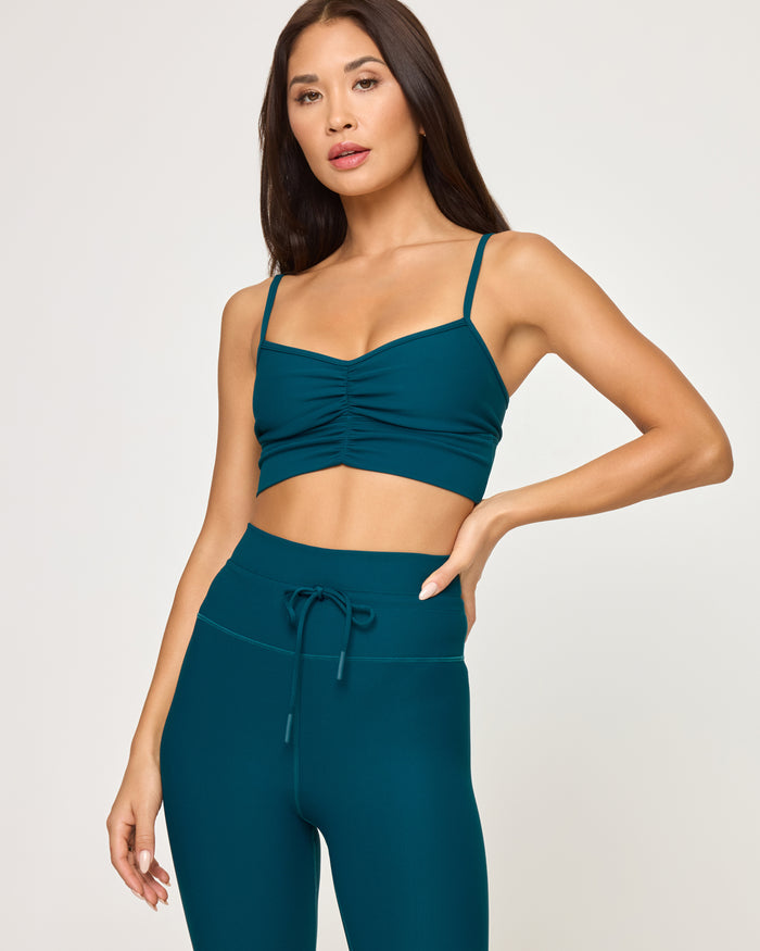 Close-up front view of model wearing the Turner Legging in deep teal showing the drawstring waistband detail, with matching deep teal Soren Top, hand on hip.