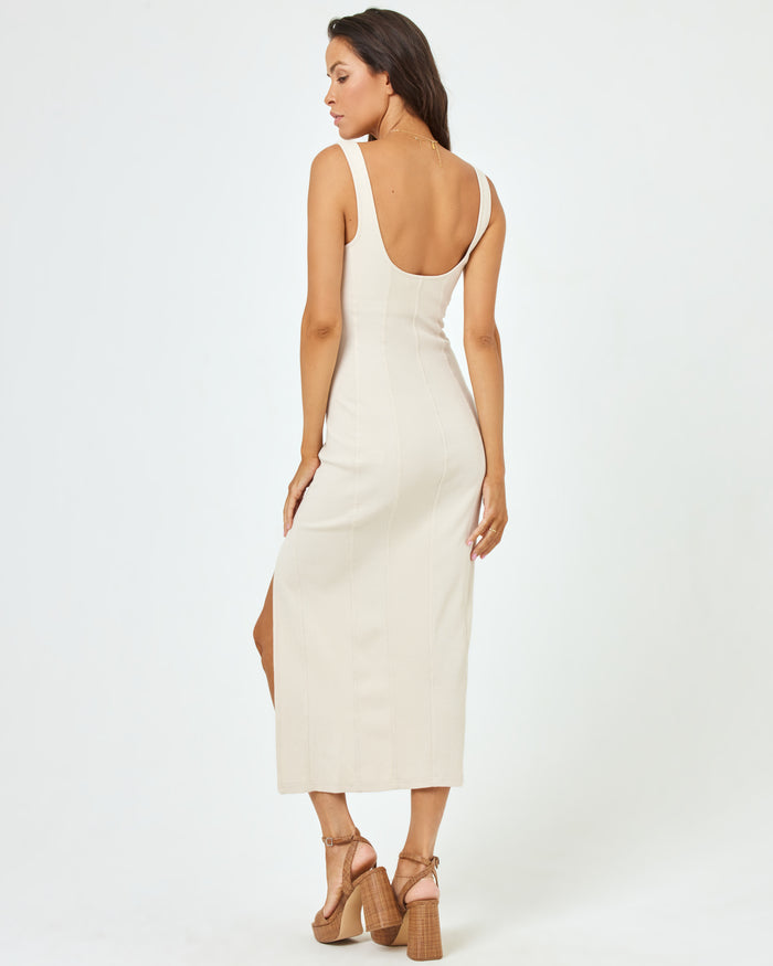 Back view of a model wearing the LSPACE Vivienne Dress in bone, a fitted midi dress with an open low back and side slit.