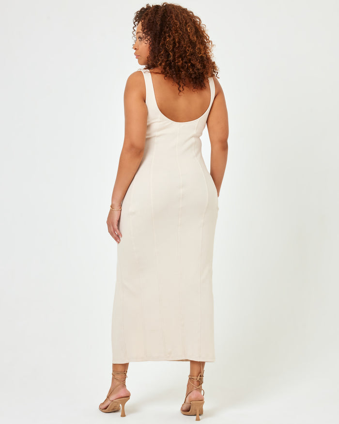 Back view of a model wearing the LSPACE Vivienne Dress in bone, a fitted midi dress with an open low back and side slit.