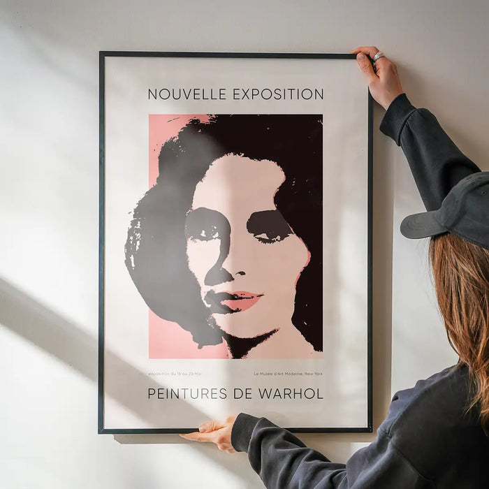 Warhol Nouvelle Exhibition Poster being hung on a wall in a black frame