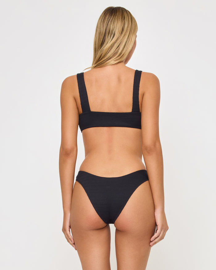 Close-up front view of a model wearing the LSPACE Willow Bikini Top in black, highlighting the center front O-ring hardware and gathered fabric detail, paired with the black Rocky Bikini Bottom.