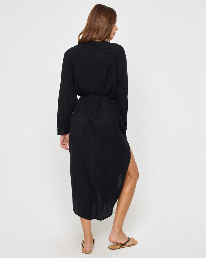 Back view of a model wearing the LSPACE Yoli Shirtdress in black, showing the full-length back of the midi shirtdress with the drawstring waist and the high-low hemline.