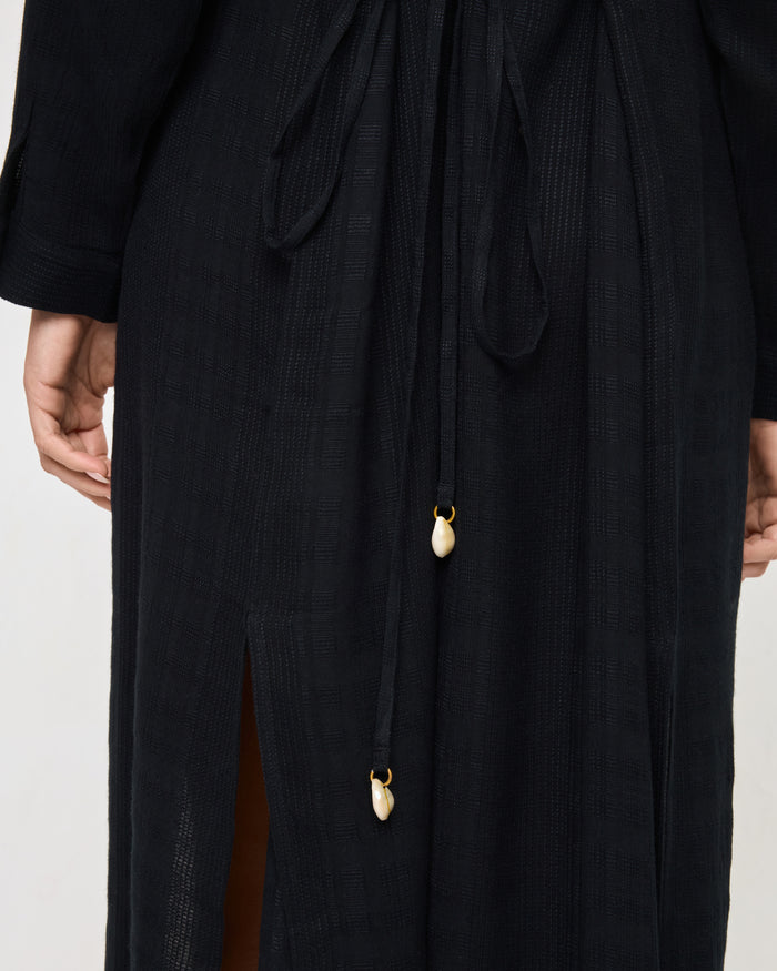 Close-up of the LSPACE Yoli Shirtdress in black, highlighting the drawstring waist tie with decorative cowrie shell charm accents.